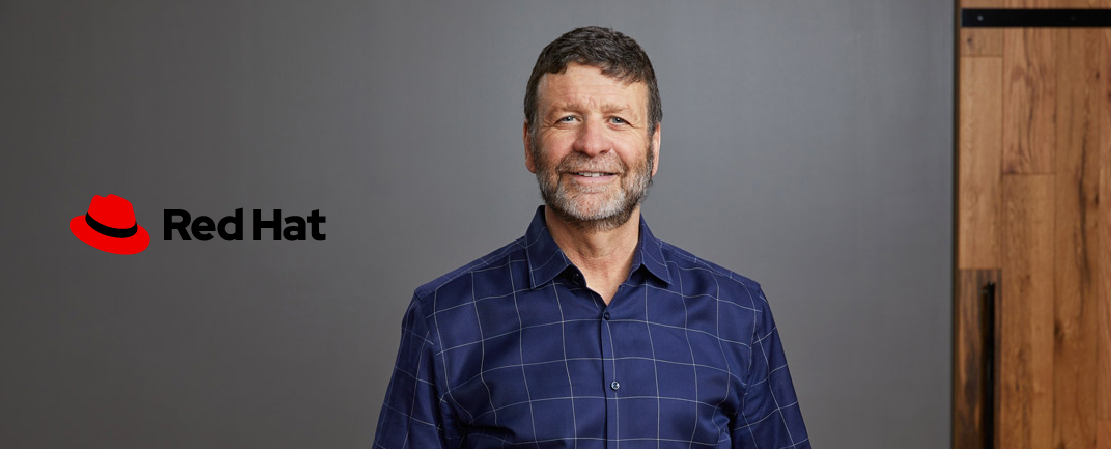 Photograph of Red Hat CEO Paul Cormier with the Red Hat logo placed on a dark gray background beside him, where it has low contrast and is difficult to see.